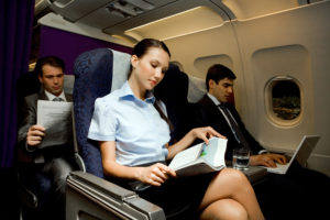 Image of pretty girl reading magazine while handsome man typing next to her in airplane