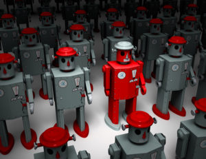 A narrow light reveals a red 1950s style tin toy robot standing out in rows of similar gray robots.